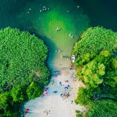 Letnie, magiczne jeziora w Polsce. Ludzie kąpią się w zielonej wodzie, odpoczywają na piaszczystej plaży otoczonej trzcinami i drzewami.