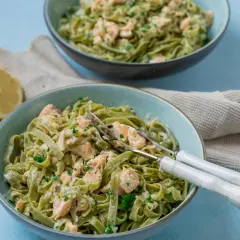 Zwei Schüsseln cremiger Tagliatelle al salmone, garniert mit Petersilie, daneben eine Zitronenhälfte und ein Küchentuch.