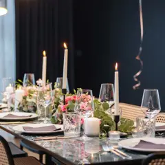Tavola apparecchiata con candele, fiori rosa e bicchieri per un elegante servizio alla francese.