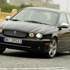 Czarny Jaguar X Type na brukowanej ulicy, z charakterystyczną atrapą chłodnicy i okrągłymi reflektorami.