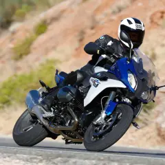 Motocyklista w kasku BMW śmiga na sportowym BMW RS 1200 po krętej drodze wśród pustynnych wzgórz.