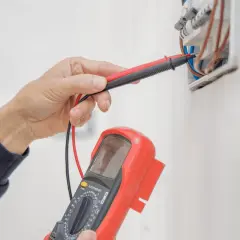 Elektryk sprawdza instalację elektryczną multimetrem, przygotowując protokół odbioru.