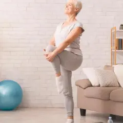 Une femme âgée sourit en faisant un exercice d'équilibre, idéal pour une fiche technique gym douce pour personne âgée.