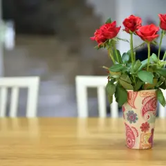 Czerwone róże w ozdobnym wazonie na drewnianym stole. Chcesz wiedzieć, co zrobić, żeby róże dłużej stały?