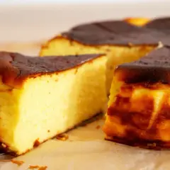 Puszysty sernik z przypieczoną skórką, pokrojony na kawałki.