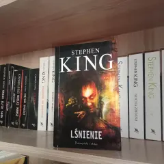 Książki Stephena Kinga na półce, w tym "Lśnienie" z przerażającą okładką.