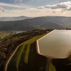 Zbiornik na szczycie góry Żar, otoczony zielonymi wzgórzami i malowniczą doliną z jeziorem i wioskami.