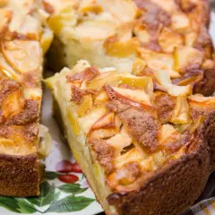 Un délicieux gâteau aux pommes, doré et moelleux, avec des morceaux de fruits caramélisés sur le dessus. Une part est déjà coupée, prête à être dégustée.