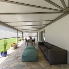 Telo per pergolato fissato con sistema a scomparsa, creando un'area relax con divano e tavolo da pranzo.