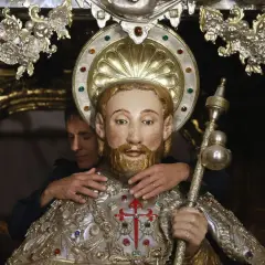 Un hombre ajusta una figura religiosa adornada, quizás preparándola para una celebración que se celebra hoy en España.