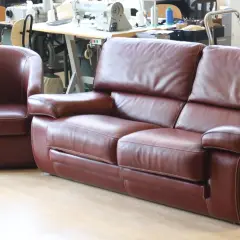 Un fauteuil et un canapé en cuir marron, avec des coutures blanches contrastantes, sont présentés dans un atelier.
