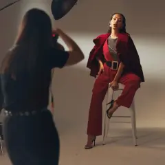 Modelka w czerwonym garniturze pozuje do zdjęcia. Fotografka pracuje, zastanawiając się, ile zarabia fotograf.