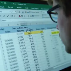 Mężczyzna w okularach analizuje dane w arkuszu kalkulacyjnym Excel. Widoczny jest fragment tabeli z kolumnami "Culeły", "Cren to Dalta Pent Relanes" i "Insaint".