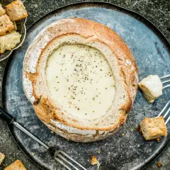 Une généreuse quantité de pain est prête à être trempée dans cette fondue savoyarde crémeuse, servie dans un pain rond.