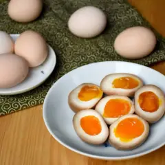 Na talerzu połówki jajek do ramenu z płynnym, pomarańczowym żółtkiem. Obok całe jajka.