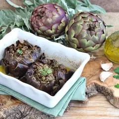 Carciofi al forno morbidi ripieni, serviti in una teglia bianca con olio d'oliva, aglio e prezzemolo.