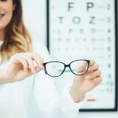 Okulary progresywne dla osób z astygmatyzmem. Optometrystka prezentuje okulary na tle tablicy Snellena.