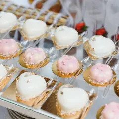 Eleganckie finger food w kieliszkach: serduszka i kwiatki w białej i różowej polewie, ozdobione perełkami i płatkami złota.