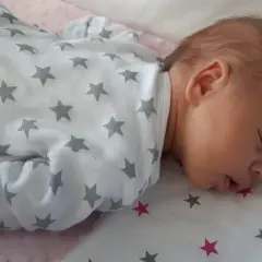Słodki noworodek śpi z otwartą buzią, ubrany w pajacyk w gwiazdki.