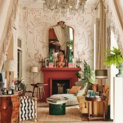 Salon éclectique avec papier peint aux figures rouges, cheminée rouge, mobilier ancien et moderne, rideaux à franges.