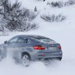Szary BMW E71 X6 z napędem na cztery koła pokonuje zaspy śnieżne, unosząc chmury białego puchu.