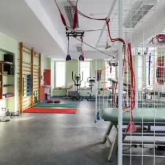Sala do rehabilitacji ambulatoryjnej: drabinki, rowery stacjonarne, materace, sprzęt do ćwiczeń zawieszenia.