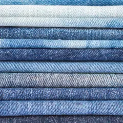 Pile de jeans bleus de différentes teintes. Le jean est fait de coton, un tissu résistant et confortable.