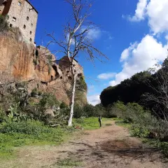 Sentiero verso Castel Sant'Elia, cosa vedere: roccia imponente, vegetazione rigogliosa e un cielo azzurro con nuvole bianche.