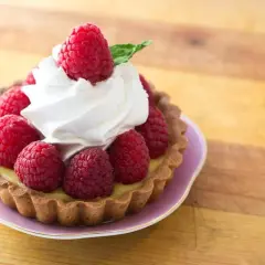 Tartelette garnie de framboises fraîches et d'une délicate crème chantilly, évoquant l'origine d'une douceur intemporelle.