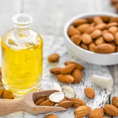 Olio di mandorle puro, ideale per la cura delle cicatrici chirurgiche, circondato da mandorle fresche.