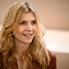 Uśmiechnięta Clémence Poésy z falującymi blond włosami i niebieskimi oczami, ubrana w brązową skórzaną kurtkę.