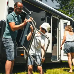 Un père et son fils sortent une chaise pliante de leur camping-car, prêts pour une aventure en Ardeche.