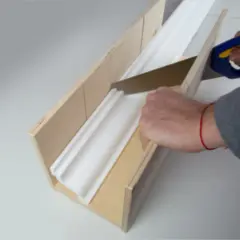 Hände sägen eine weiße Styroporleiste mit einer Gehrungslade zu, um sie später anbringen zu können.