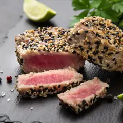 Apetyczny stek z tuńczyka w sezamie, idealnie wysmażony, z kawałkami limonki i natką pietruszki.