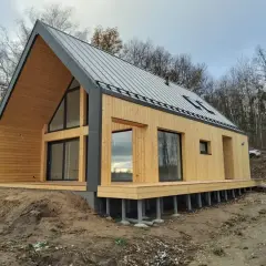 Nowoczesny dom pasywny z drewnianą elewacją i dużymi oknami, otoczony lasem.
