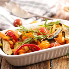 Un plato blanco lleno de coloridas verduras al horno, con romero fresco y tomates cherry.