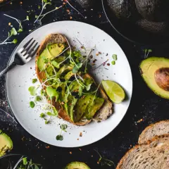 Tost z awokado, kiełkami i limonką na talerzu, obok pieczywo i awokado. Pyszne i zdrowe śniadanie, idealne dla zasad zdrowego stylu życia.