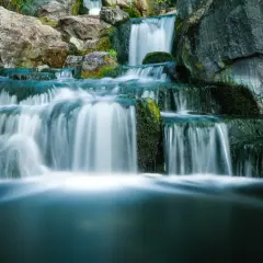 Serene waterfall photography captures cascading water flowing over moss-covered rocks, creating a tranquil, misty scene.