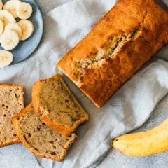 Pyszny chlebek bananowy z dwóch bananów, pokrojony na kromki. Obok leżą świeże banany i talerzyk z plasterkami.