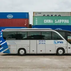 Biały autobus z napisem "Linia Nauka Jazdy" stoi na tle kontenerów. Chcesz wiedzieć, jakie prawo jazdy na busa? Ta szkoła jazdy oferuje kursy na kategorie od AM do D1.