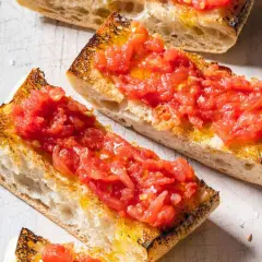 Rebanadas de pan tostado cubiertas con tomate rallado y aceite de oliva, un delicioso pan tumaca.