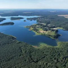 Malownicze jezioro Niesłysz otoczone lasami, z widocznymi wysepkami i zabudowaniami na brzegu.