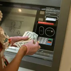 Une personne avec des gants roses prépare un dépôt d'argent liquide à un guichet automatique.