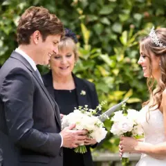 Cérémonie de mariage : une marraine émue lit une citation pour sa filleule rayonnante, entourées de fleurs.
