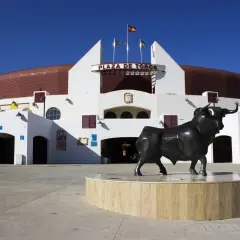 Escultura de toro frente a la Plaza de Toros Roquetas de Mar, bajo un cielo azul intenso.