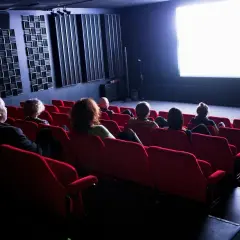 Publiken sitter i röda biosalongsstolar och tittar på en ljus bioduk. Klara biografen är redo för filmvisning.