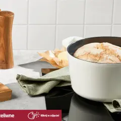 Biały garnek żeliwny z upieczonym chlebem, obok deska z masłem i młynki do przypraw.