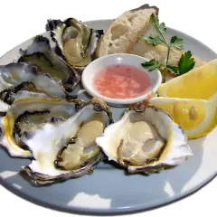 Ostra marisco fresco servida en plato con limón, pan y salsa rosada.