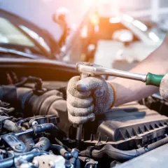 Mechanik w rękawicach dokręca śrubę kluczem nasadowym w silniku samochodu. Może to być naprawa po problemach po płukance silnika.