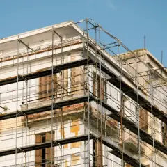 Bâtiment en rénovation, échafaudages pour aide ravalement façade sans isolation extérieur. Le ciel est bleu.